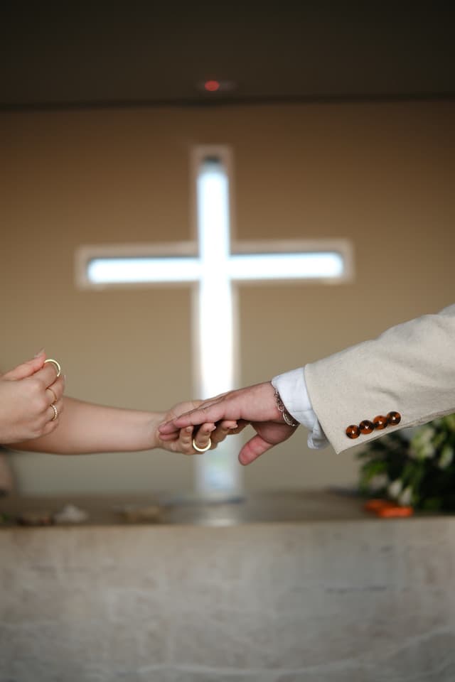 Mãos dadas dos noivos diante da cruz
